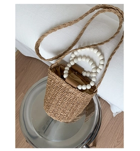 Detail of a brown woven bucket bag with distinctive white bead handles and shoulder strap