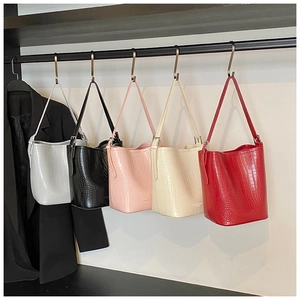Detail view of five colors of crocodile pattern bucket bags hanging on a rack