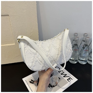 Close-up of a white textured crescent bag with fringe details and a leather strap