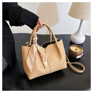 Detail of beige tote bag with grain texture, decorative silk scarf, and detachable strap