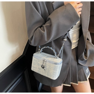 Macro shot of light blue tweed box bag featuring flower charm and woven chain strap