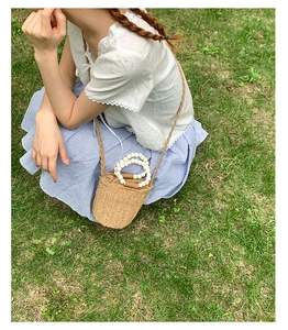 Detail of straw woven bucket bag with white bead handle on green grass background