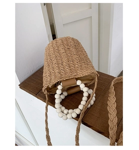 Detail of hand-woven straw bucket bag featuring a beaded handle and long shoulder strap