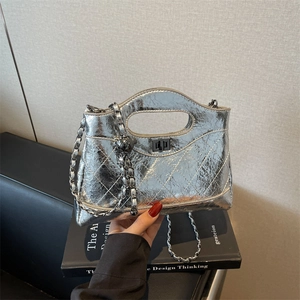 Silver quilted metallic handbag with chain strap and top handle held against grey wall