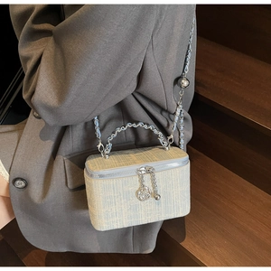 Close-up of woven tweed texture with chain strap and camellia metal charm detail