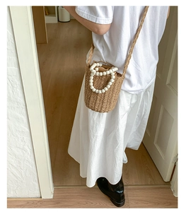 Detail of woven straw bucket bag with white bead handle and crossbody strap on a model