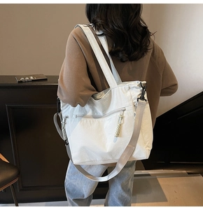 Detail view of large white canvas tote bag with woven zipper pull and crossbody strap