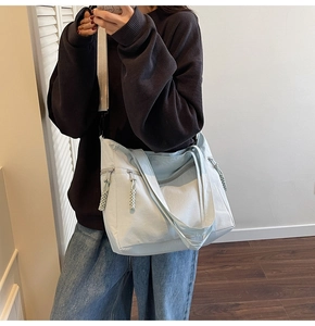 Close-up of light blue nylon tote bag with multiple zip pockets and woven zipper pulls