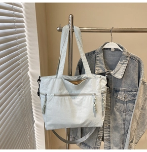 Detail of light blue canvas tote bag showing zipper pockets and woven pullers on hanger