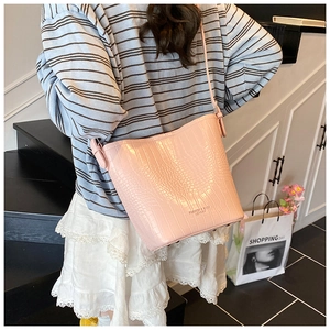 Detail of pink crocodile embossed leather bucket bag with fashion lettering and long strap