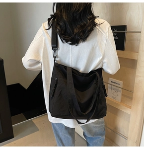 Close-up of black canvas tote bag showing side zipper detail and adjustable shoulder strap