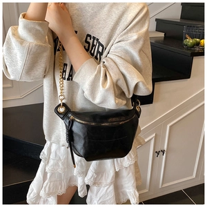 Close-up of black half-moon waist bag with gold chain strap and leather tassel detail
