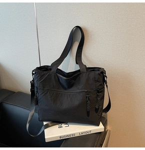 Detail of black nylon tote bag featuring front dual zipper pocket and adjustable strap
