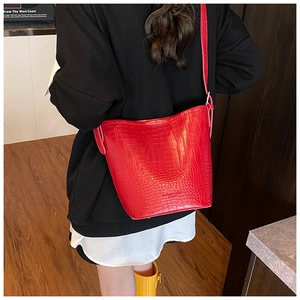 Detail of red crocodile texture bucket bag with thin strap shown on a model's back