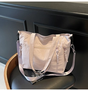 Detail of pink nylon tote bag with pleated texture and woven rope zipper on a black chair
