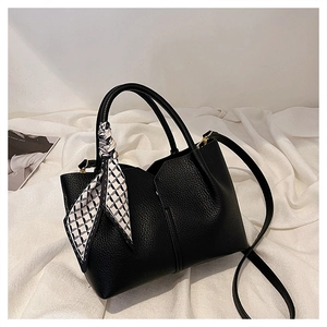 Detail of black lychee leather tote bag with decorative silk scarf and golden metal buckles