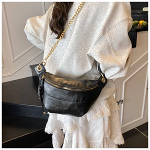 Detail view of the black crossbody chest bag with golden chain strap on a model