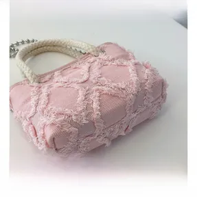 Détail du sac en toile rose avec texture frangée et poignée tissée blanche