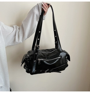 Détail du sac en cuir verni noir avec fermetures éclair argentées et sangles à oeillets