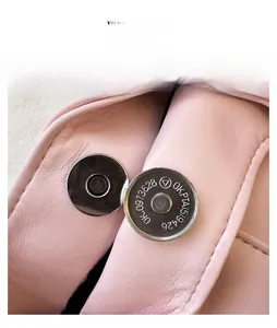 Close-up of a silver magnetic snap button on a pink leather handbag with fine grain texture