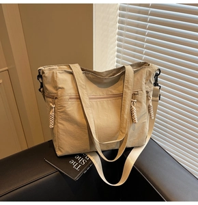 Detail of beige nylon tote bag featuring metal zippers and adjustable woven strap