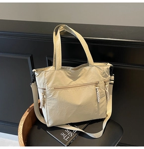 Detail of beige nylon tote bag featuring thick braided rope zipper pulls and front pocket