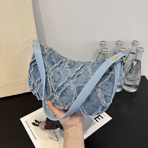 Light blue denim handbag with quilted diamond pattern and leather strap in hand