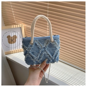 Détail du sac en denim bleu avec motif à losanges effilochés et bandoulière chaîne