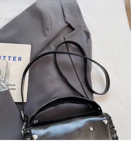 Detail of black pleated shoulder bag with heart rivets on a grey blazer backdrop