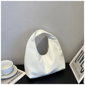Detailed view of white pleated cloud bag with unique knotted handle on a modern tabletop