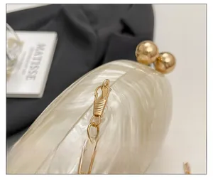 Detailed close-up of golden spherical clasp and metal chain on pearlescent acrylic clutch