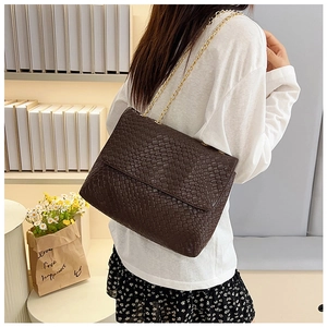 Close-up of deep brown woven leather bag with gold chain strap worn by a model