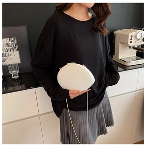 Detailed view of an oval shell evening bag with white matte finish and golden chain