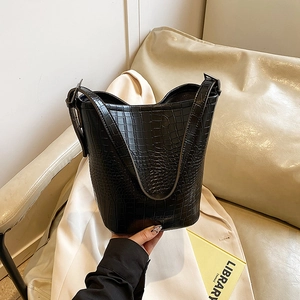 Large black crocodile-textured bucket bag with adjustable strap on a leather sofa