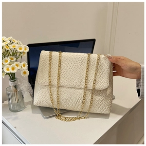 White woven shoulder bag with gold chain strap shown in a lifestyle office setting