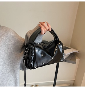 Detail of glossy black handbag with heart rivets and ruffles held by a model