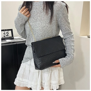 Detail of black woven texture and gold chain strap on a chic crossbody flap bag