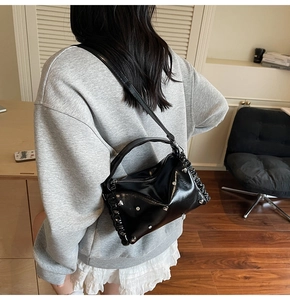 Detailed view of black patent leather bag with silver studs on model shoulder