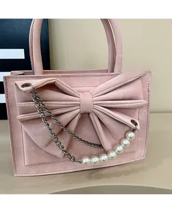 Detailed view of pink satchel with oversized bow, metal chain, and faux pearl strap decoration