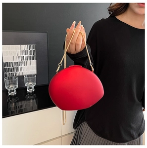 Detail of red oval acrylic clutch bag with fine gold metal chain held by a model