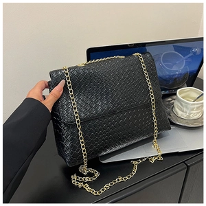 Close-up of black woven texture handbag with golden chain strap on a desk