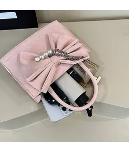 Pink suede handbag with bow and pearl chain detail showing spacious interior capacity