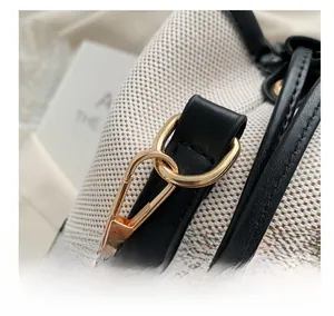 Close-up of polished gold-tone metal hook and contrast leather trim on a canvas bucket bag