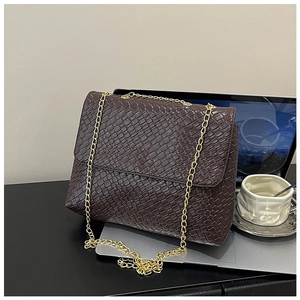 Close-up of deep brown woven leather bag with gold chain strap next to a laptop