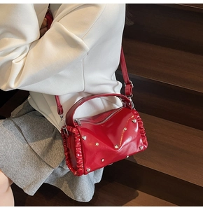 Detail of red patent leather handbag with ruffled edges and silver heart stud accents