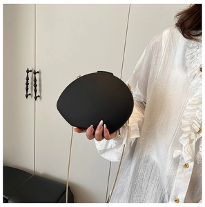 Detail of a matte black oval clutch bag with a delicate gold chain on a model