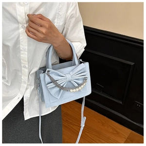 Detail of light blue bow handbag featuring silver chains and elegant pearl accents