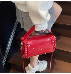 Detailed view of red glossy leather bag featuring heart rivets and side pleats