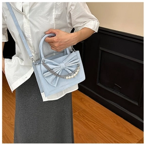 Detail of light blue bow handbag featuring elegant pearl and metal chain decoration