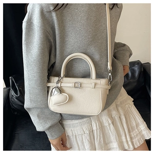 Close-up of cream lychee leather handbag with heart charm and metal buckle detail